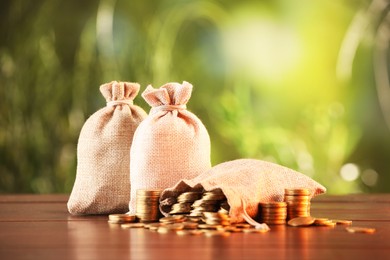 Photo of Burlap bags and stacked coins on wooden table against blurred background