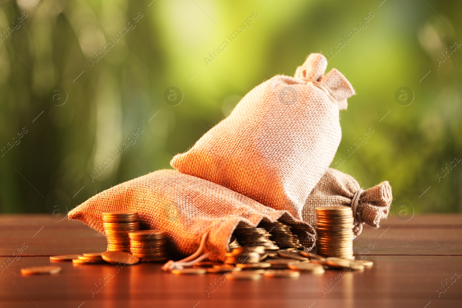Photo of Burlap bags and stacked coins on wooden table against blurred background