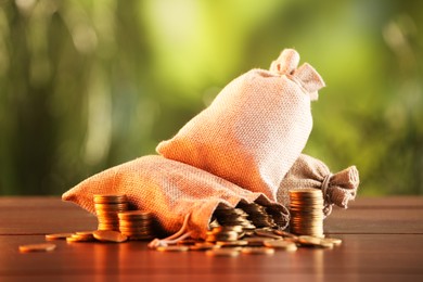 Photo of Burlap bags and stacked coins on wooden table against blurred background
