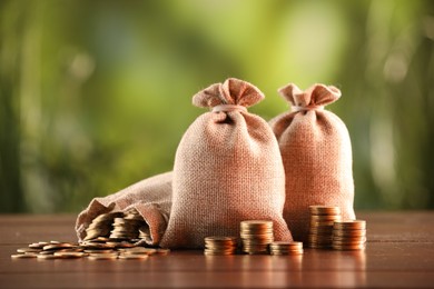 Photo of Burlap bags and stacked coins on wooden table against blurred background