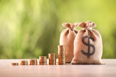 Photo of Burlap bags and stacked coins on table against blurred background