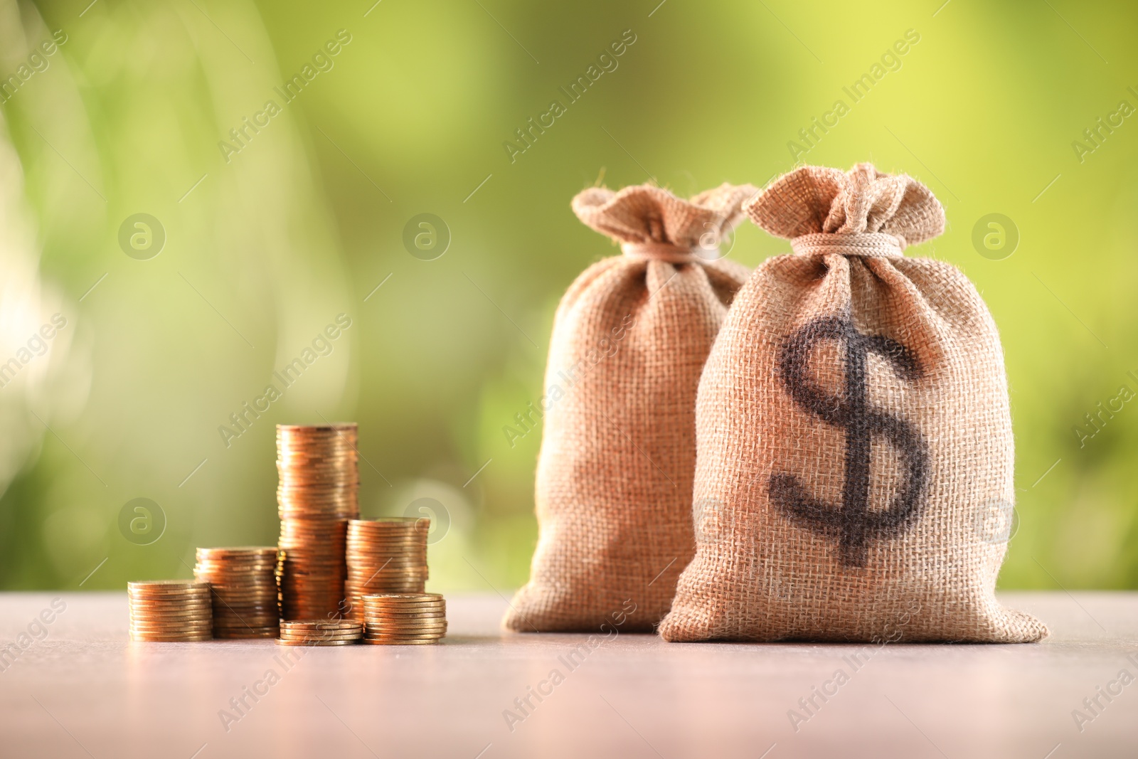 Burlap bags and stacked coins on table against blurred background Photo of Burlap bags and stacked coins on table against blurred background