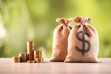Photo of Burlap bags and stacked coins on table against blurred background
