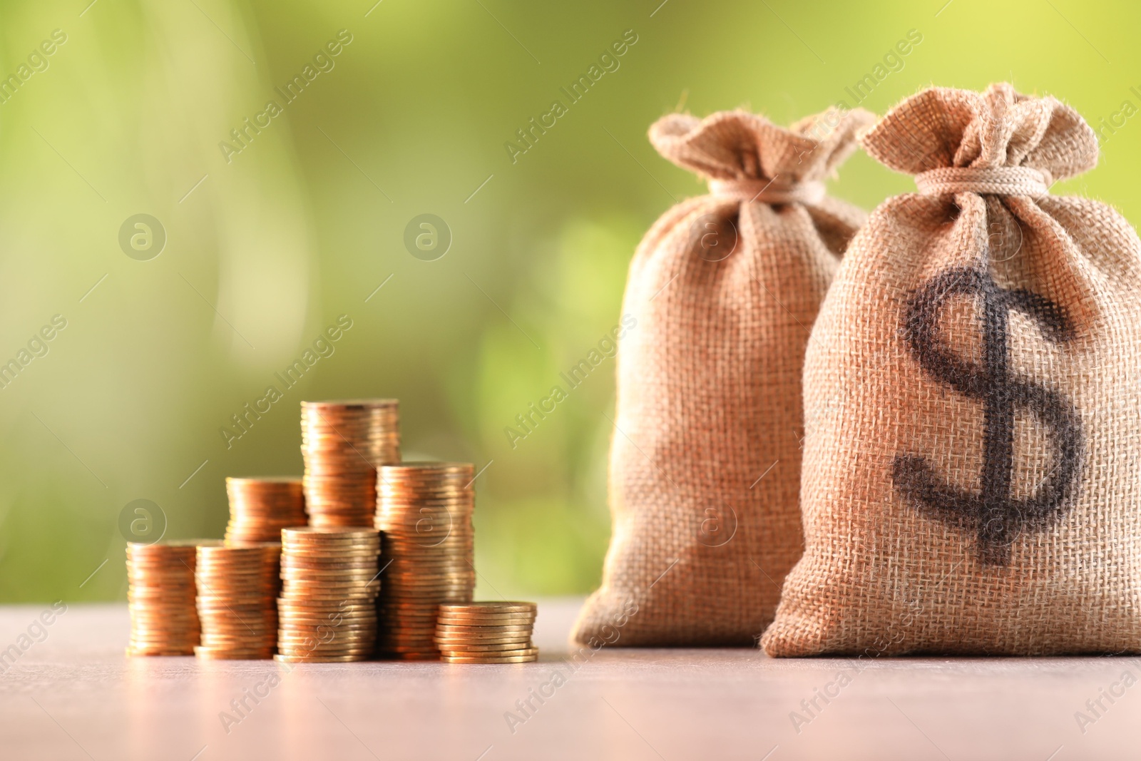 Burlap bags and stacked coins on table against blurred background Photo of Burlap bags and stacked coins on table against blurred background