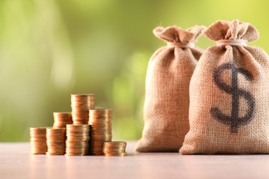 Photo of Burlap bags and stacked coins on table against blurred background