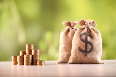 Photo of Burlap bags and stacked coins on table against blurred background