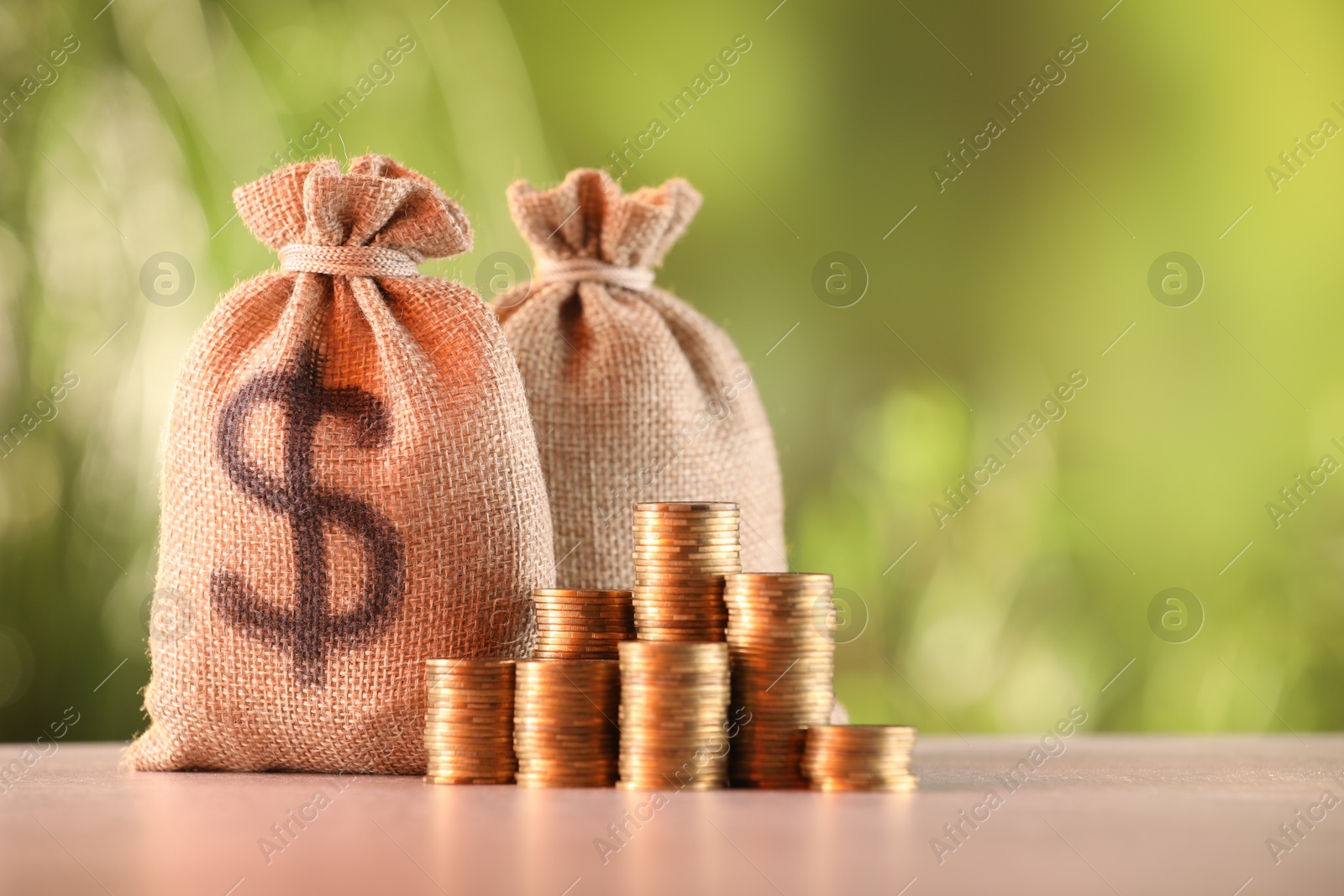 Burlap bags and stacked coins on table against blurred background, space for text Photo of Burlap bags and stacked coins on table against blurred background, space for text