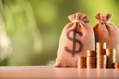 Photo of Burlap bags and stacked coins on table against blurred background, space for text