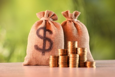 Photo of Burlap bags and stacked coins on table against blurred background