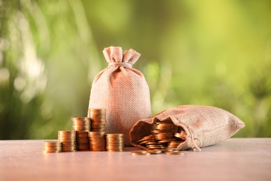 Photo of Burlap bags and stacked coins on table against blurred background