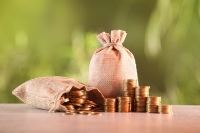 Photo of Burlap bags and stacked coins on table against blurred background