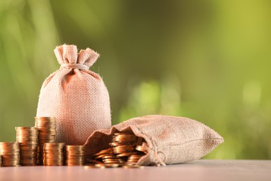 Photo of Burlap bags and stacked coins on table against blurred background