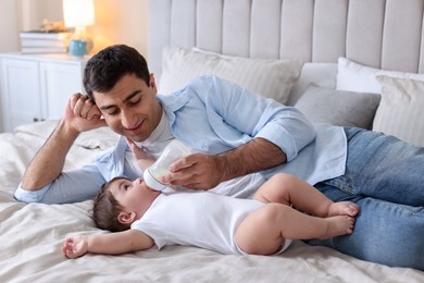 Photo of Father feeding his little baby with bottle on bed at home