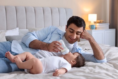 Photo of Father feeding his little baby with bottle on bed at home
