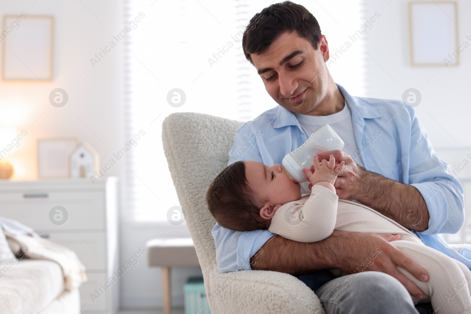 Father feeding his little baby with bottle on armchair at home. Space for text Photo of Father feeding his little baby with bottle on armchair at home. Space for text