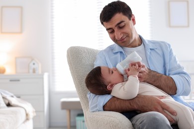 Photo of Father feeding his little baby with bottle on armchair at home. Space for text