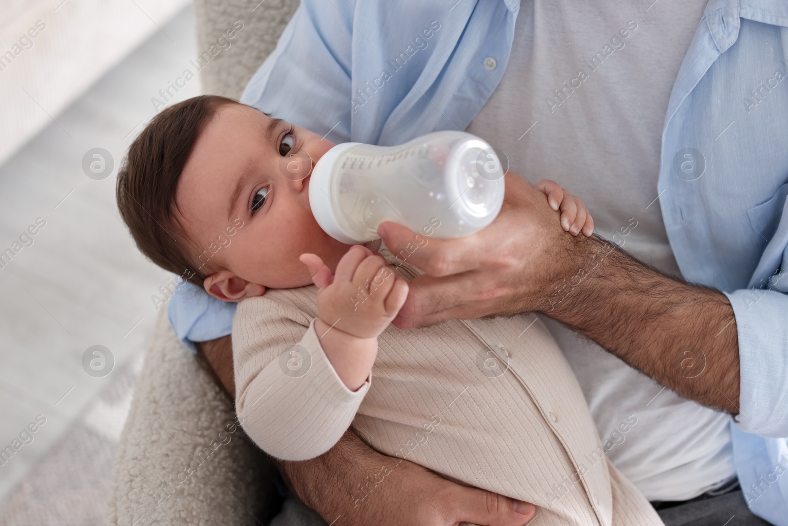 Photo of Father feeding his little baby with bottle on armchair at home, closeup