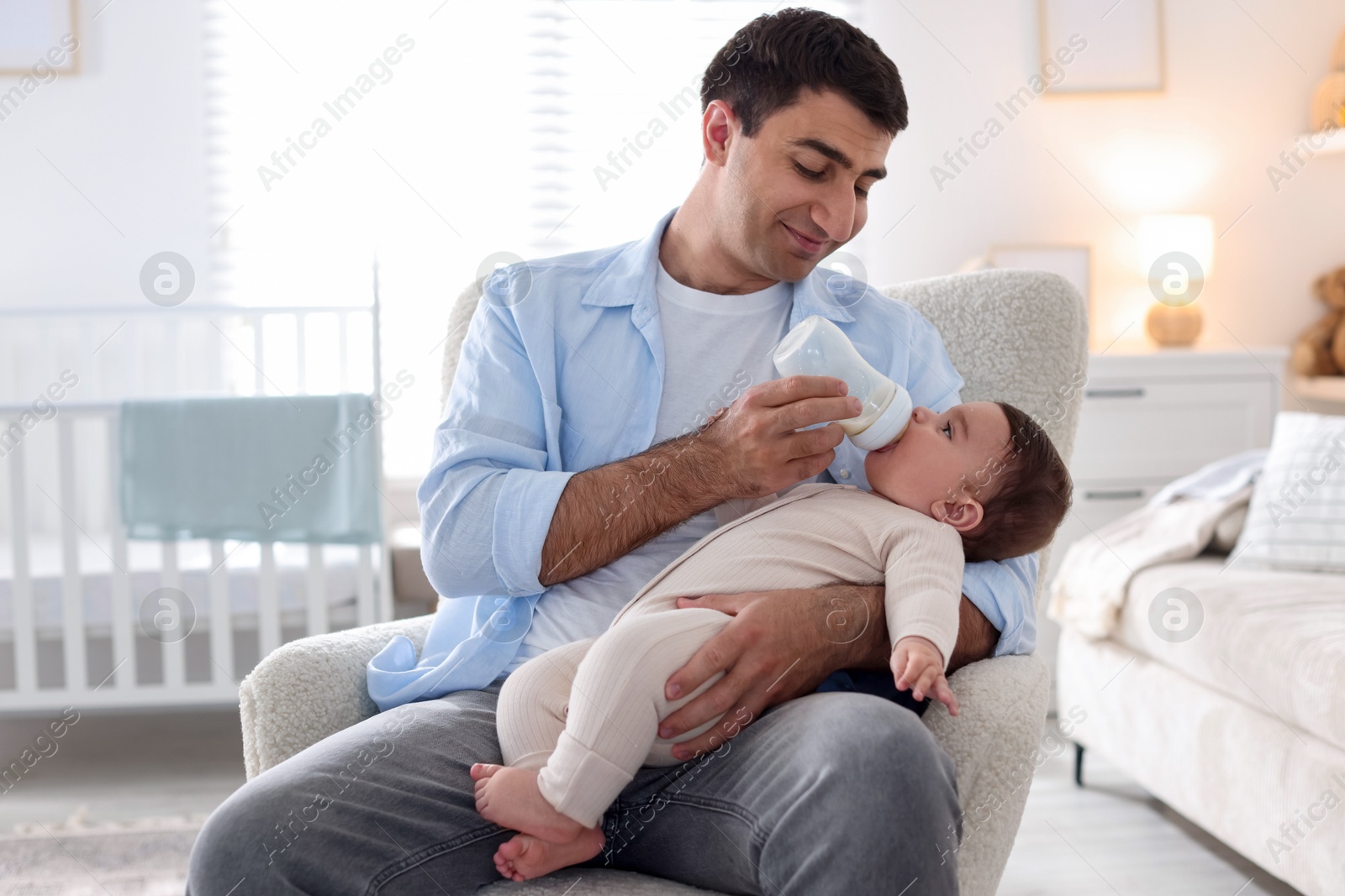 Father feeding his little baby with bottle on armchair at home Photo of Father feeding his little baby with bottle on armchair at home