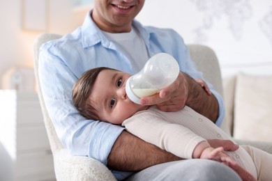 Photo of Father feeding his little baby with bottle on armchair at home, closeup