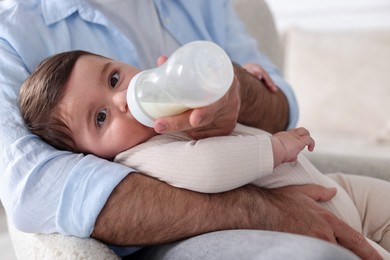 Photo of Father feeding his little baby with bottle on armchair at home, closeup
