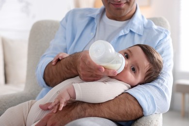 Photo of Father feeding his little baby with bottle on armchair at home, closeup