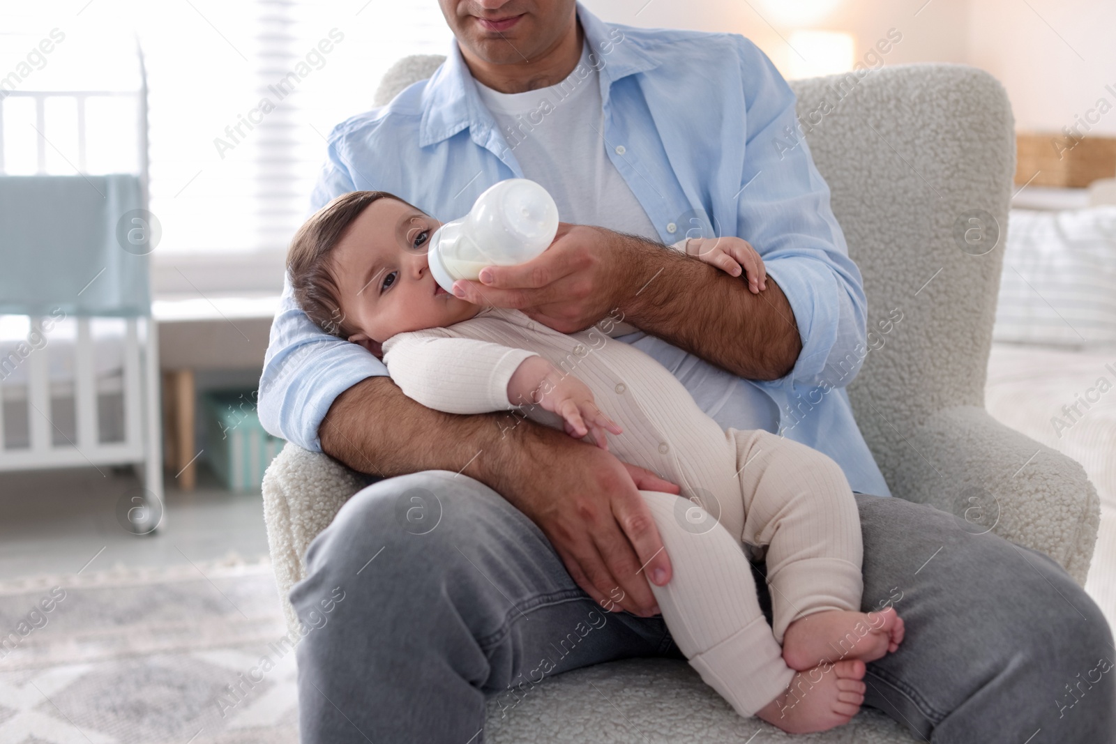 Father feeding his little baby with bottle on armchair at home, closeup Photo of Father feeding his little baby with bottle on armchair at home, closeup