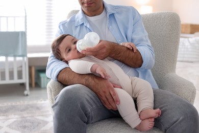 Photo of Father feeding his little baby with bottle on armchair at home, closeup