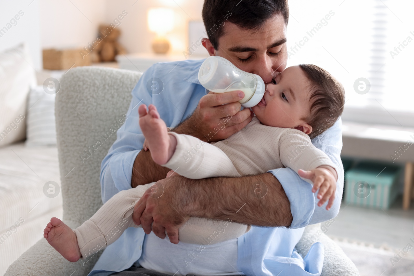 Father feeding his little baby with bottle on armchair at home Photo of Father feeding his little baby with bottle on armchair at home
