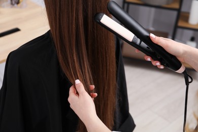 Photo of Hairdresser straightening woman's hair in salon, closeup