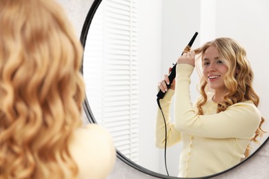 Photo of Woman curling her hair near mirror indoors