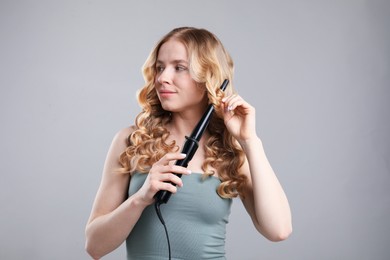 Photo of Woman curling her hair on grey background