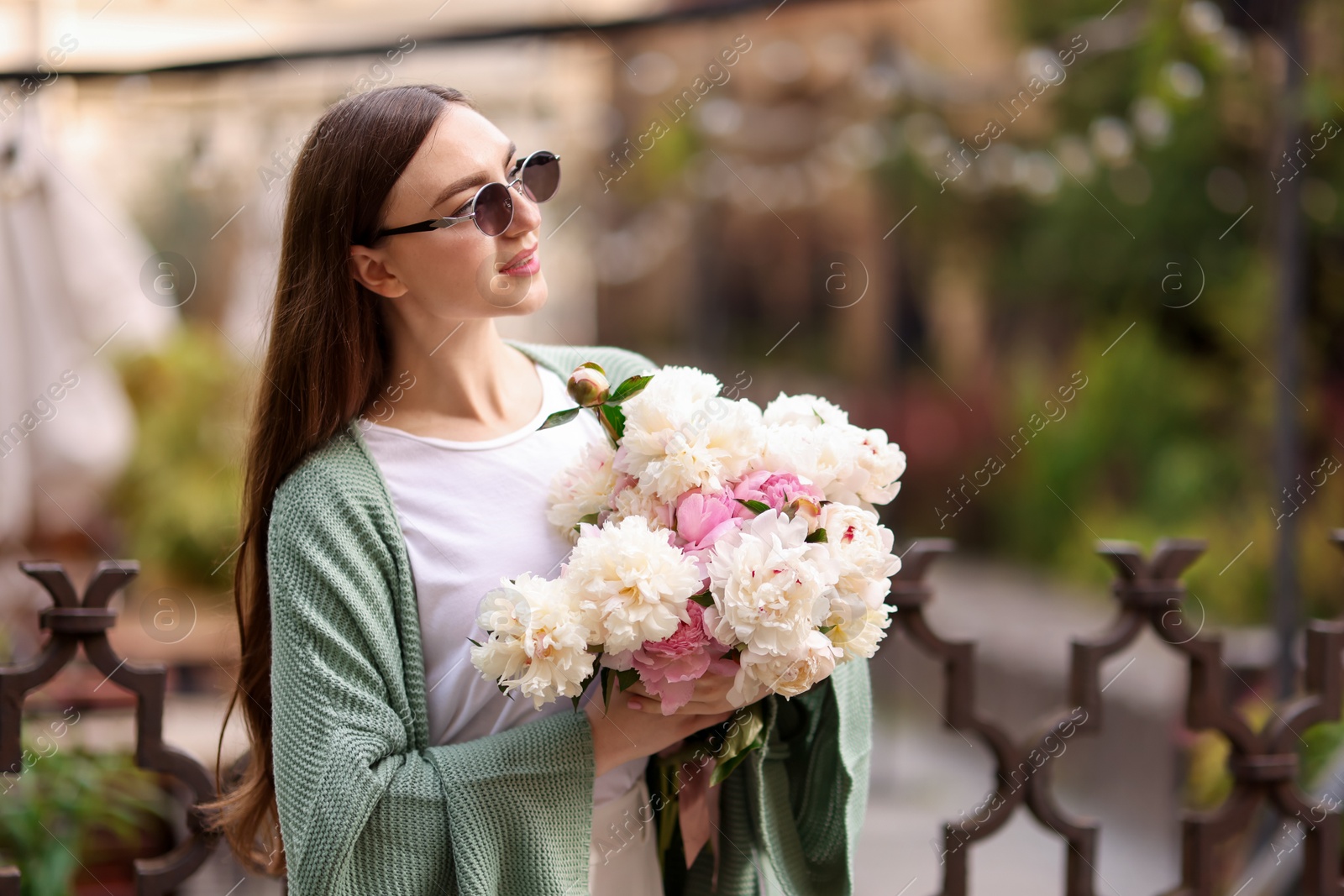Charming woman with bouquet of beautiful peonies on city street. Space for text Photo of Charming woman with bouquet of beautiful peonies on city street. Space for text