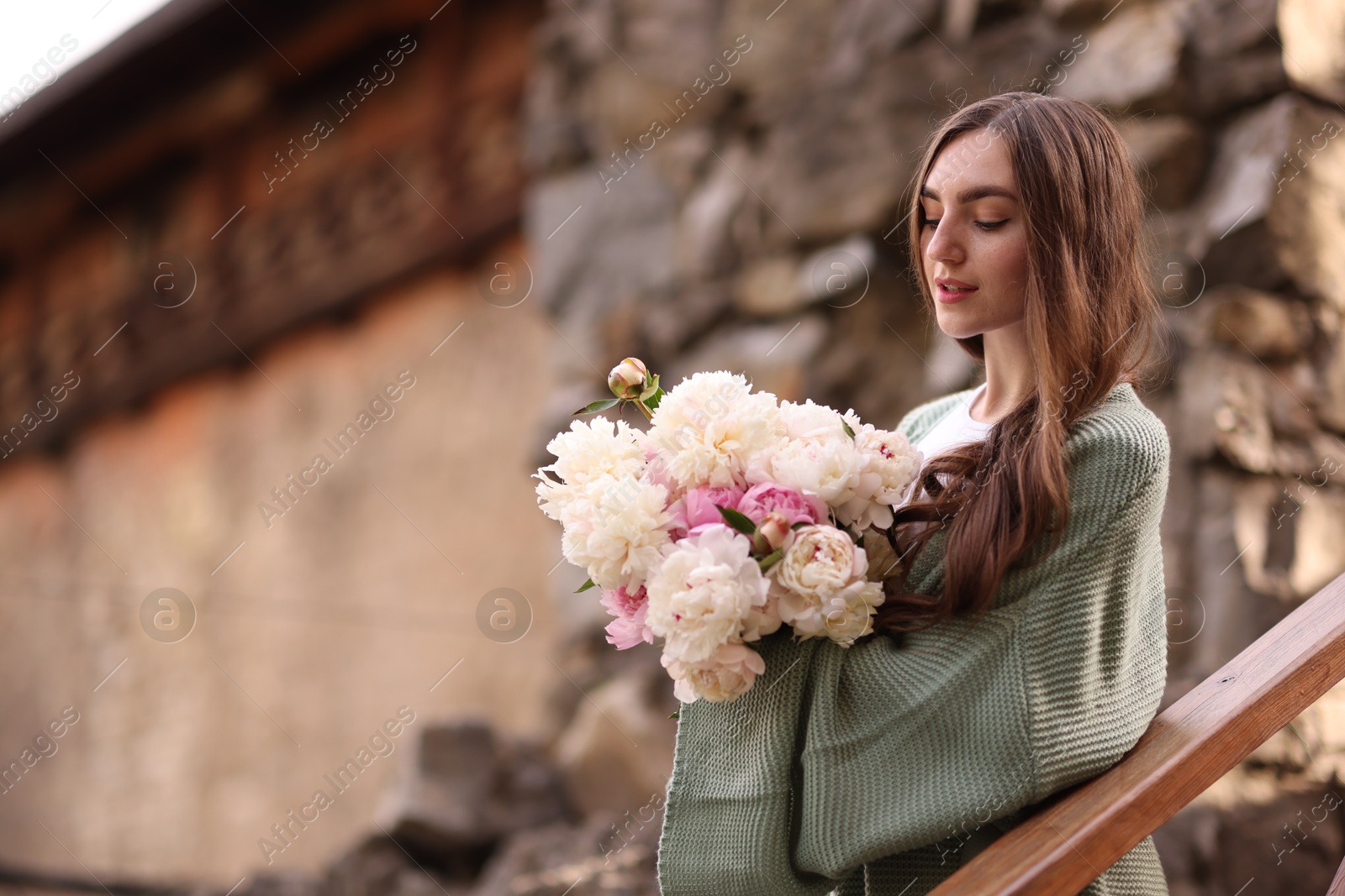 Charming woman with bouquet of beautiful peonies on city street. Space for text Photo of Charming woman with bouquet of beautiful peonies on city street. Space for text
