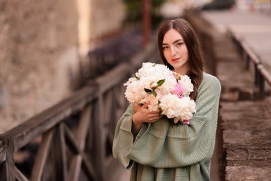 Photo of Charming woman with bouquet of beautiful peonies on city street. Space for text
