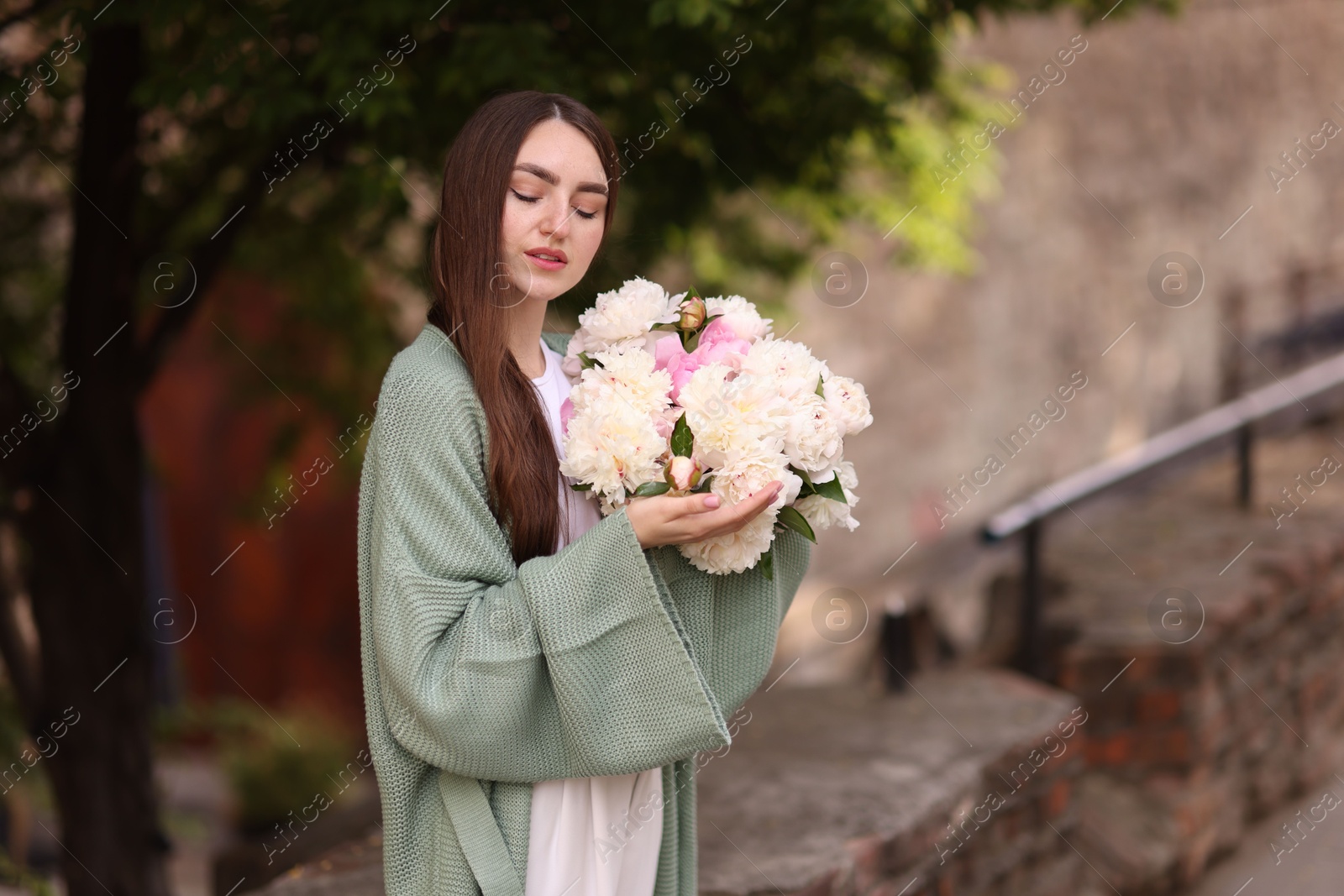 Charming woman with bouquet of beautiful peonies on city street. Space for text Photo of Charming woman with bouquet of beautiful peonies on city street. Space for text