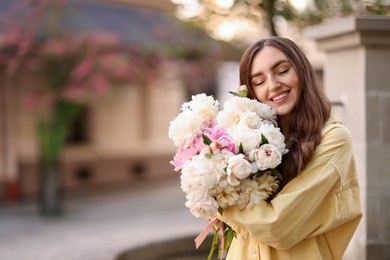 Photo of Woman with bouquet of beautiful peonies on city street. Space for text