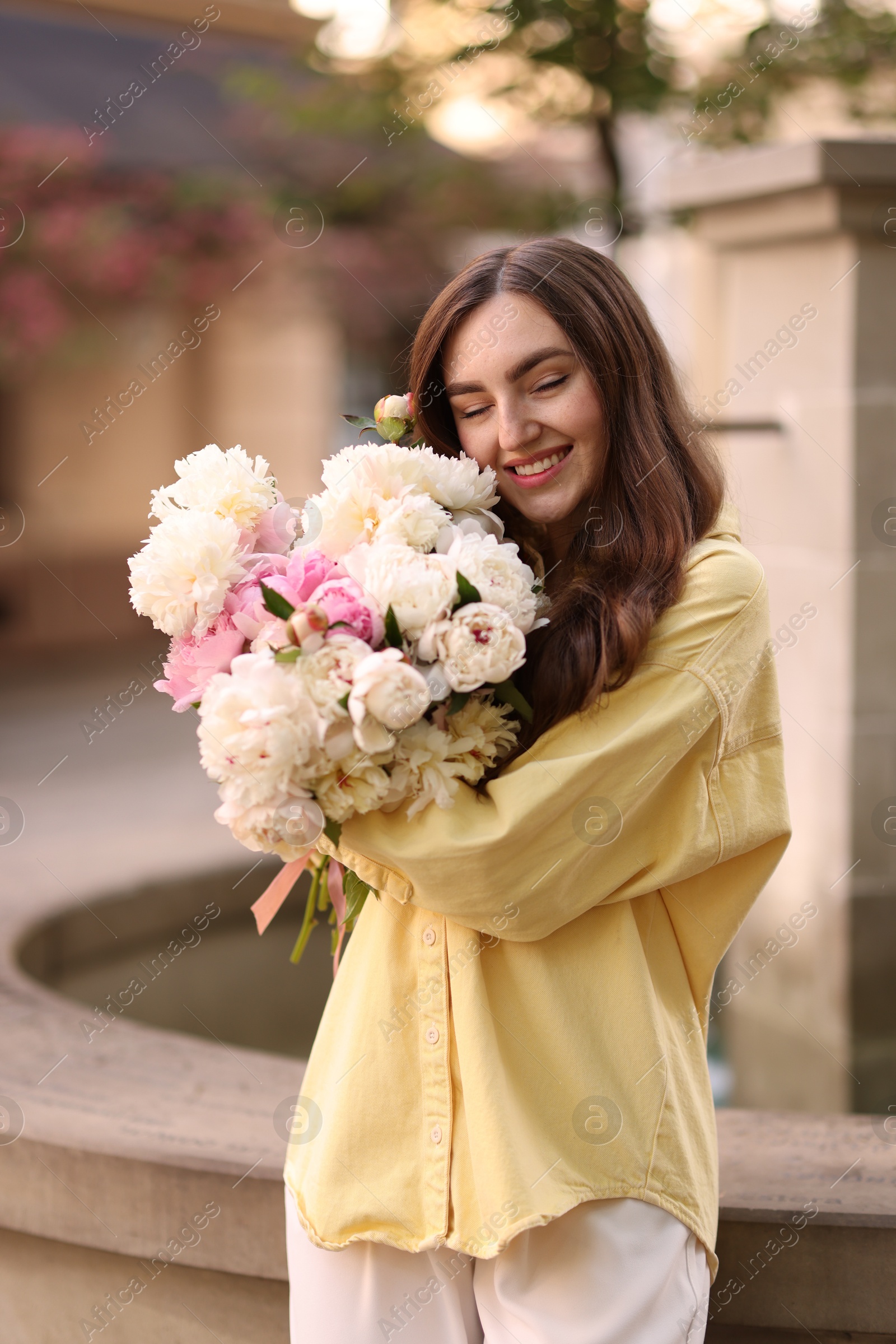 Woman with bouquet of beautiful peonies on city street Photo of Woman with bouquet of beautiful peonies on city street