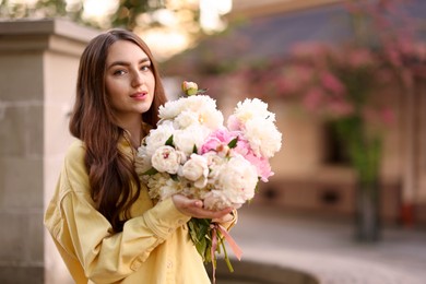 Photo of Woman with bouquet of beautiful peonies on city street. Space for text
