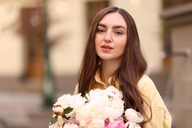 Photo of Woman with bouquet of beautiful peonies on city street. Space for text