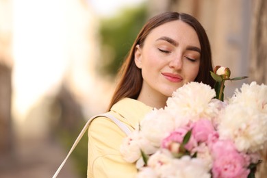 Photo of Woman with bouquet of beautiful peonies on city street. Space for text
