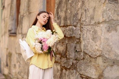 Photo of Woman with bouquet of beautiful peonies on city street. Space for text