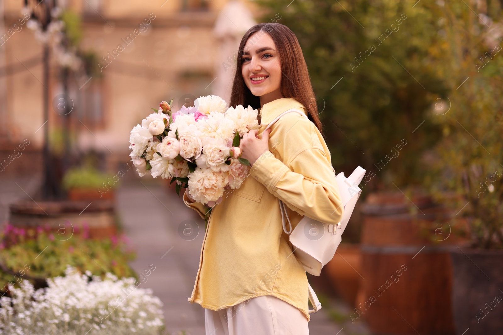 Woman with bouquet of beautiful peonies on city street Photo of Woman with bouquet of beautiful peonies on city street