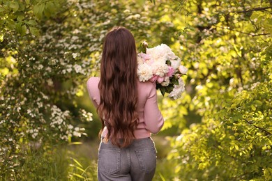 Photo of Beautiful woman with bouquet of peonies in park, back view
