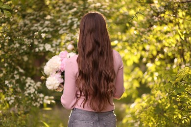 Photo of Beautiful woman with bouquet of peonies in park, back view