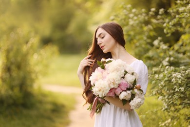 Photo of Beautiful woman with bouquet of peonies in park. Space for text