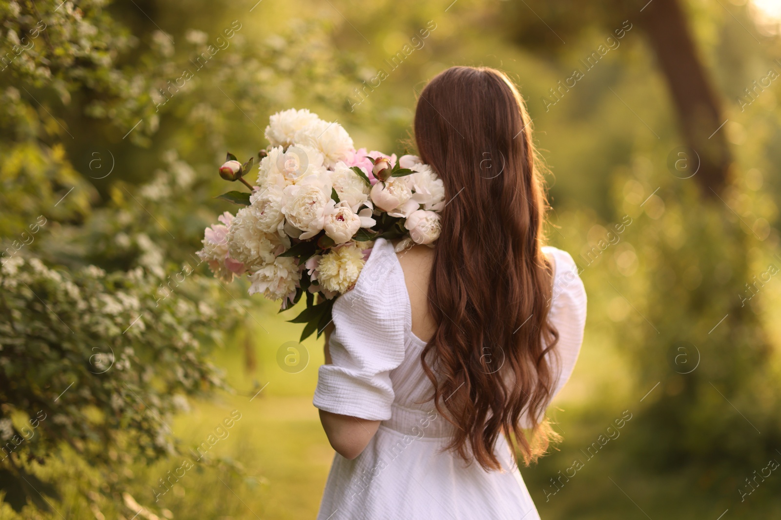 Photo of Beautiful woman with bouquet of peonies in park, back view
