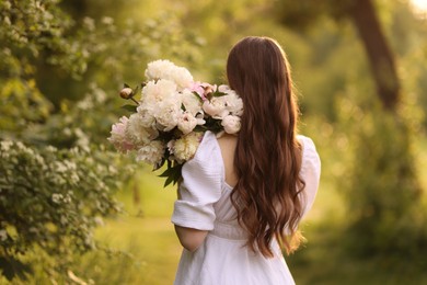Photo of Beautiful woman with bouquet of peonies in park, back view