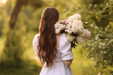Photo of Beautiful woman with bouquet of peonies in park, back view