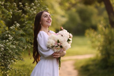 Photo of Beautiful woman with bouquet of peonies in park. Space for text