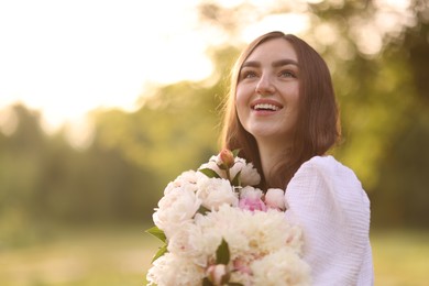 Photo of Beautiful woman with bouquet of peonies in park on sunny day. Space for text
